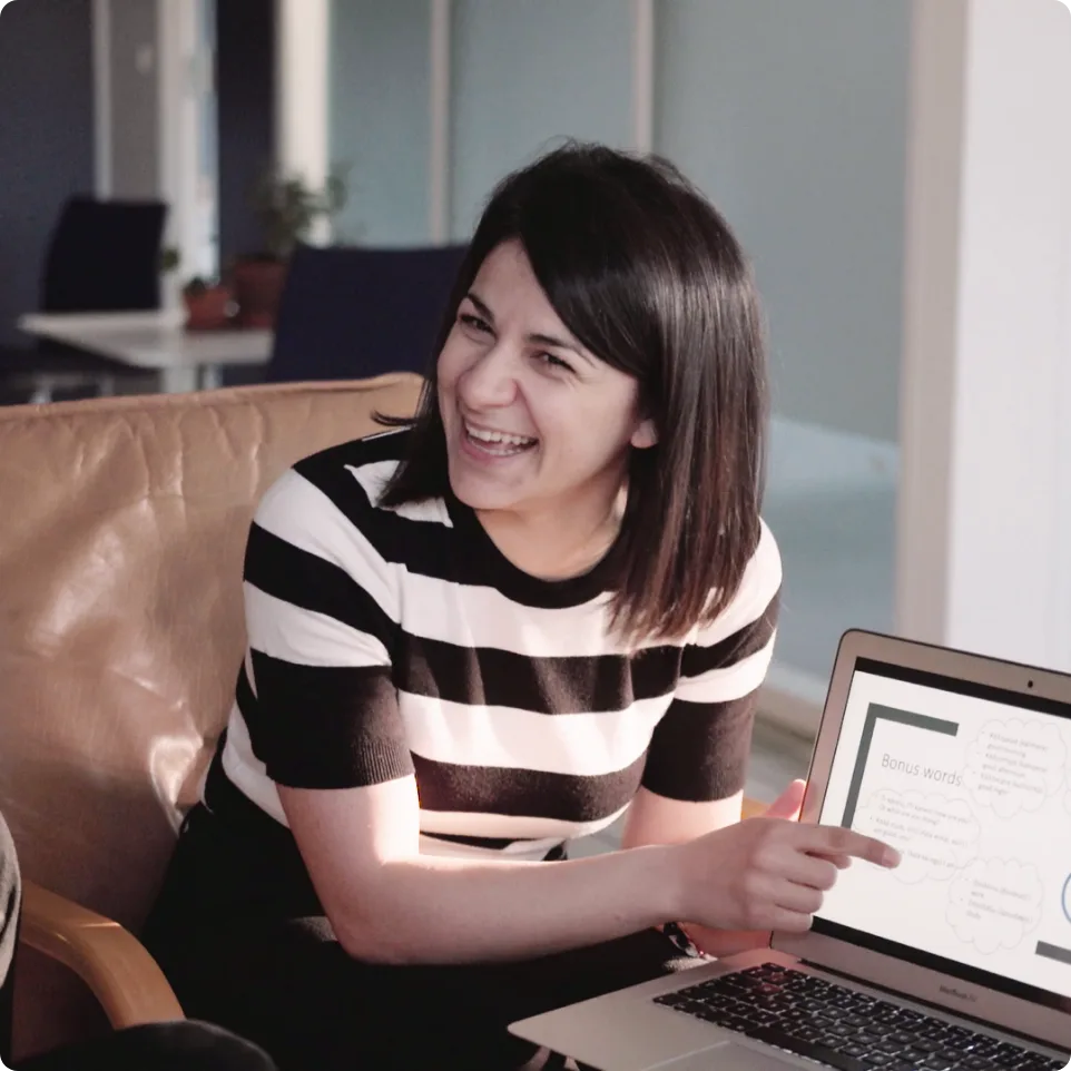 A Swap Language teacher laughing during an online lesson, pointing at a “Bonus words” slide on her laptop