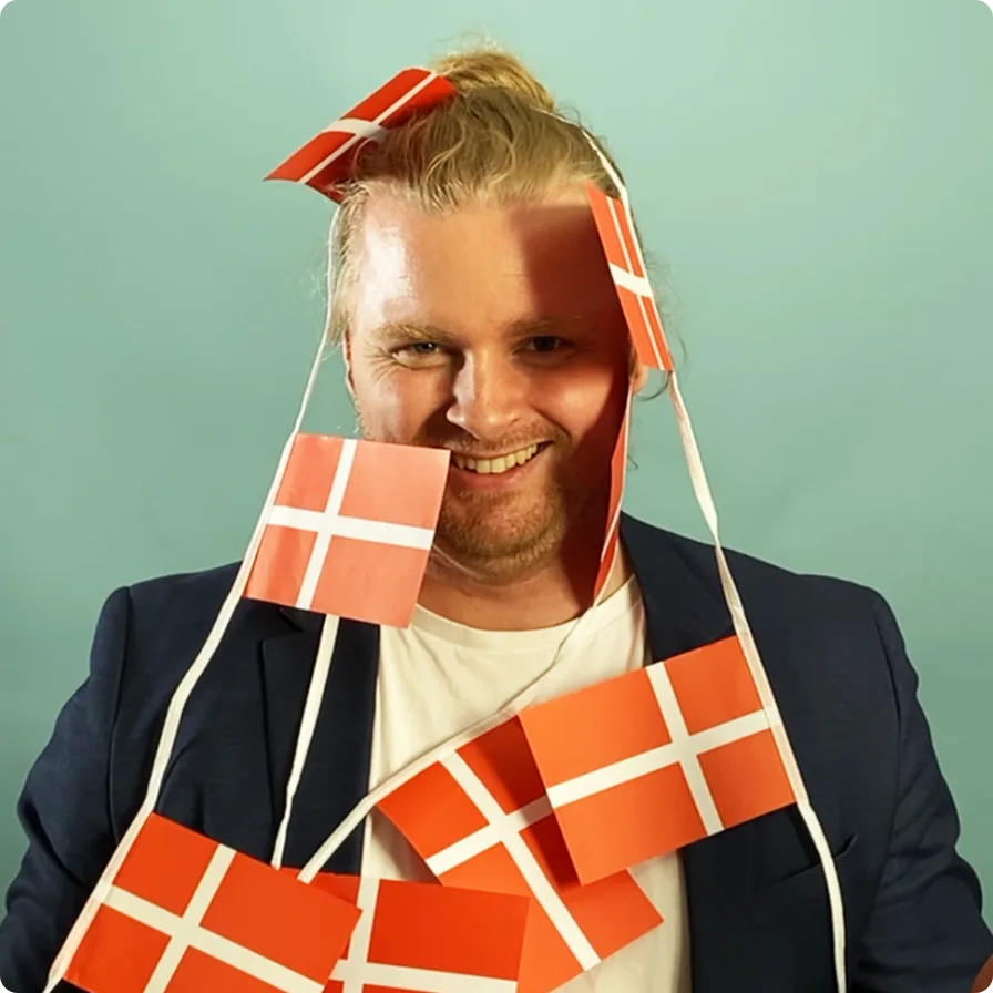 A smiling Swap Language colleague draped in a string of small Danish flags