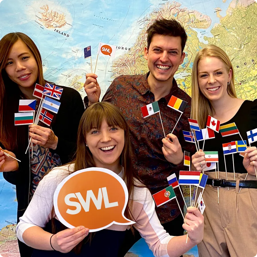 Four Swap Language colleagues in front of a world map, holding paper flags from many countries and a Swap Language speech-bubble sign