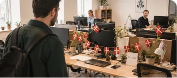 A row of office desks decorated with small Danish flags while colleagues work
